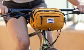 Close-up of All-City Turntable Sling Bag mounted on bike handlebars, person riding