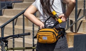 Person wearing All-City Turntable Sling Bag as lumbar pack next to bike, putting u-lock in bag