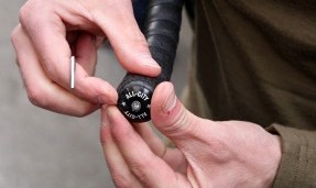 Persons hands putting black All-City Lock-On Bar Plug on black handlebars top view