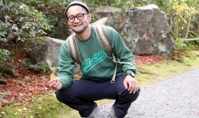 Person wearing a green throwback crewneck sweatshirt while squatting outdoors