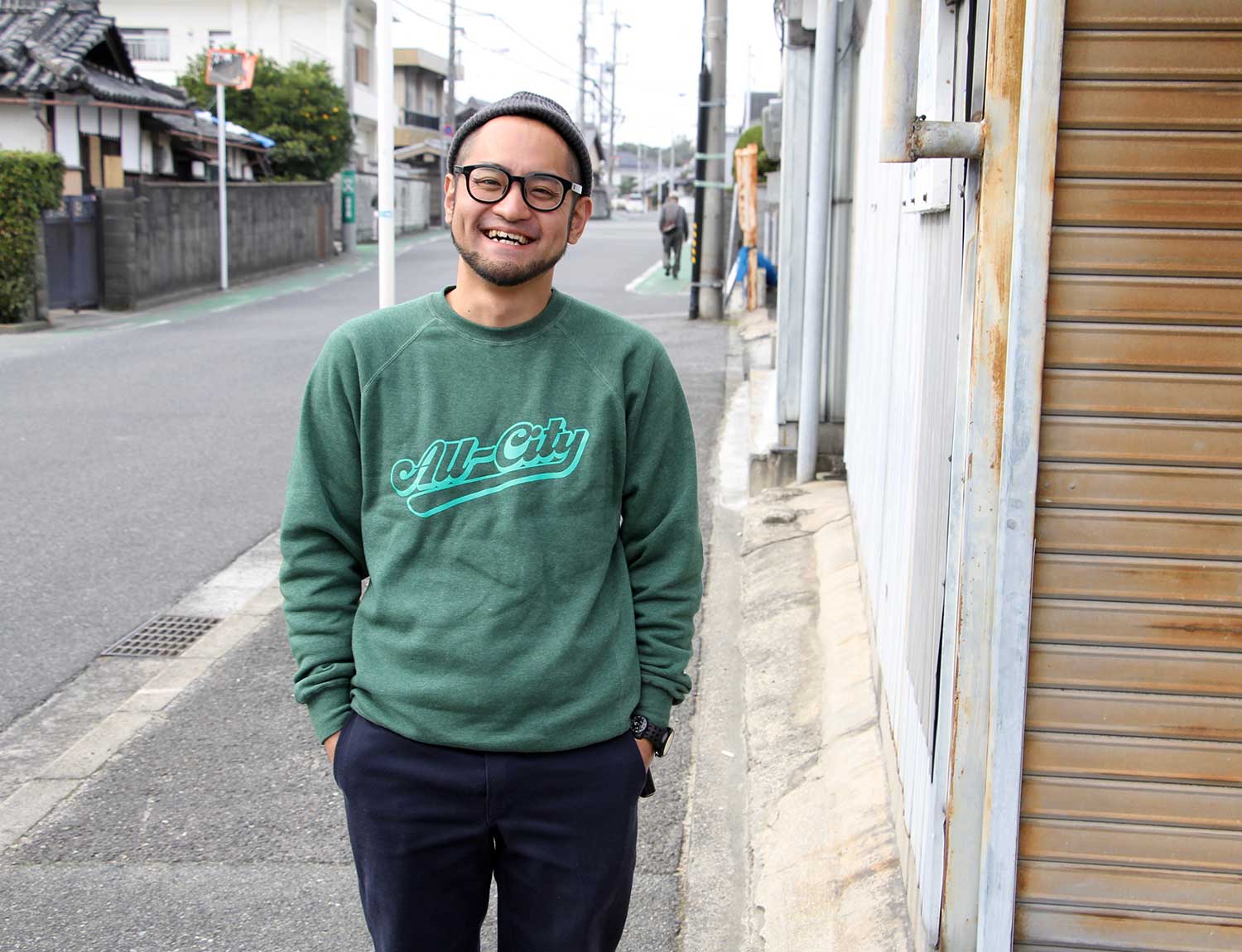 Person wearing a green throwback crewneck sweatshirt with a street background
