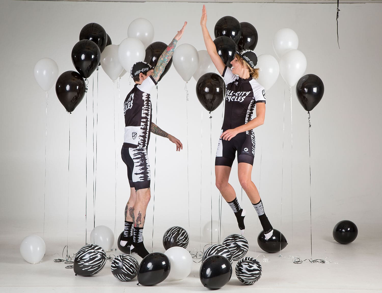 Two people wearing All-City black and white Wangaaa Bibs with black and white balloons around them 