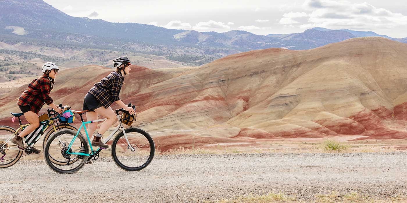 Two cyclists riding Gorilla Monsoon bikes up remote desert gravel road in the mountains, out of the saddle