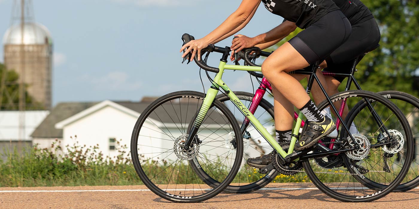 Two cyclist riding Zig Zag bikes on country road wearing cycling apparel ride side by side